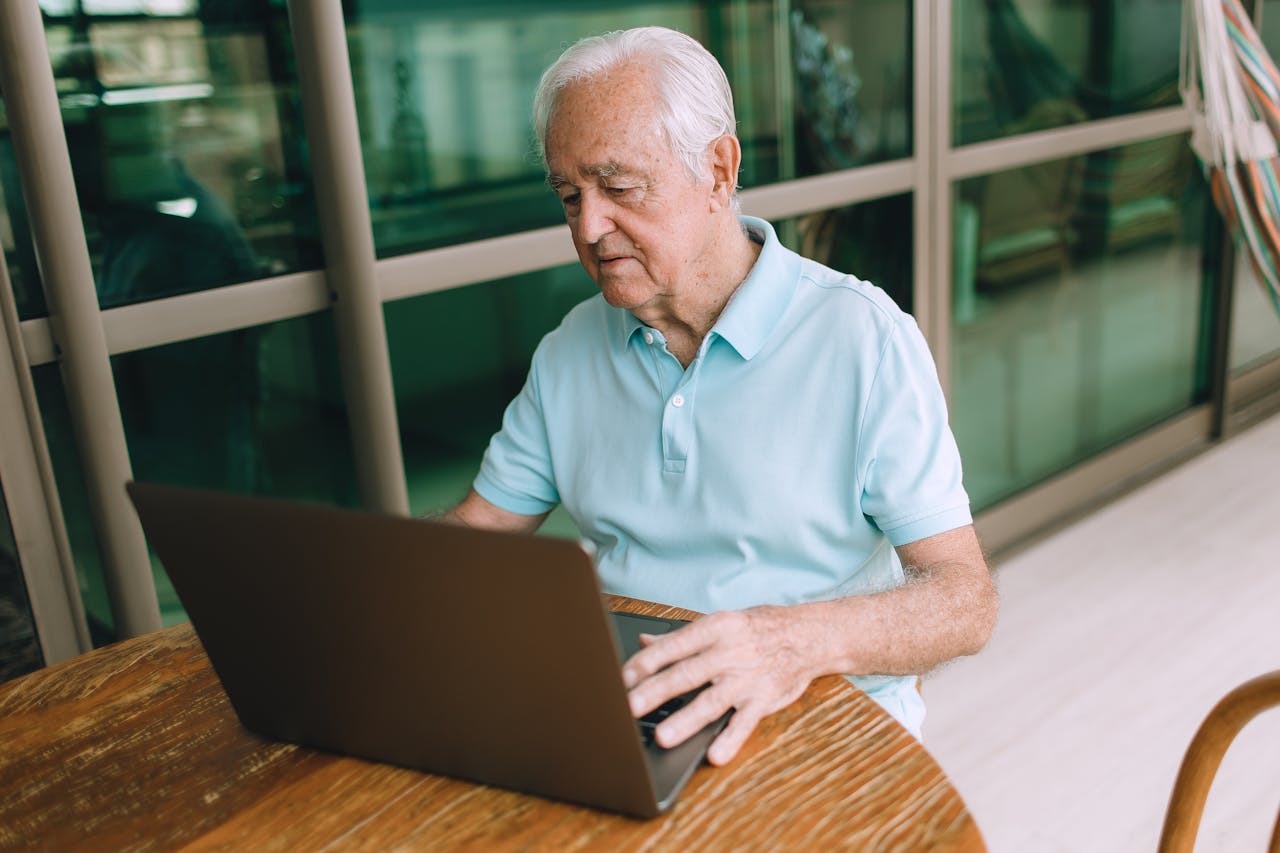 An elderly man focused on using a laptop indoors, highlighting technology and connectivity.