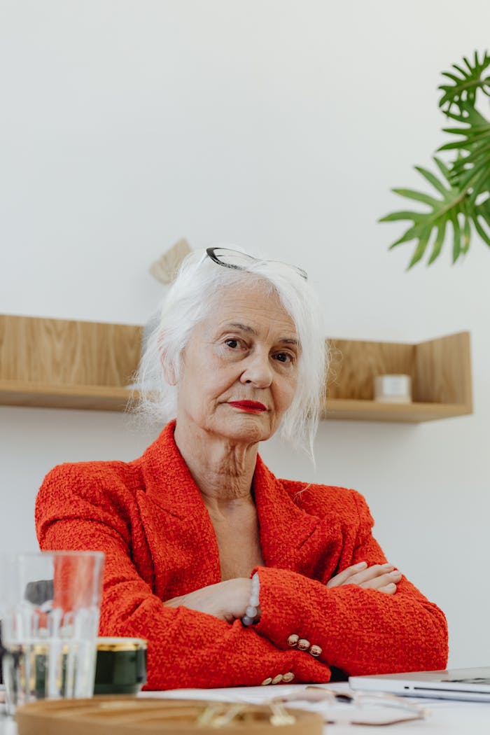 Confident senior businesswoman in a red suit seated in a modern office setting.