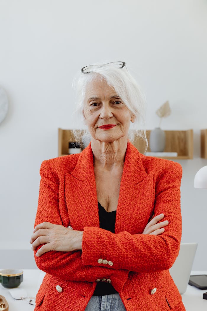 Senior businesswoman in red blazer confidently poses in modern office. Ideal for corporate and professional themes.
